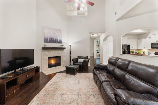 18823 Cove Mill Ln, Cypress, TX 77433 - living room featuring ceiling fan, dark wood-style flooring, a fireplace with flush hearth, a high ceiling, and arched walkways