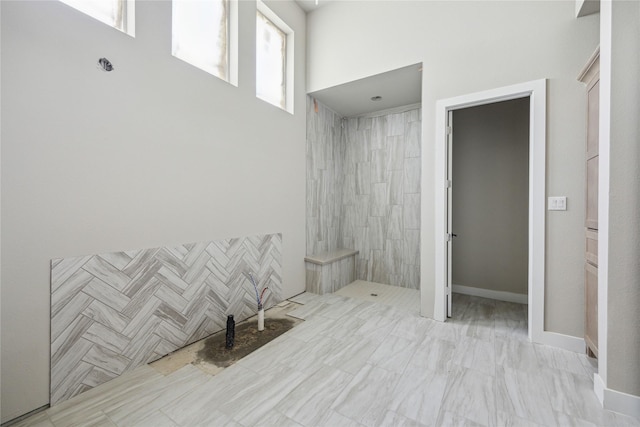 full bath with marble finish floor, a towering ceiling, and tiled shower