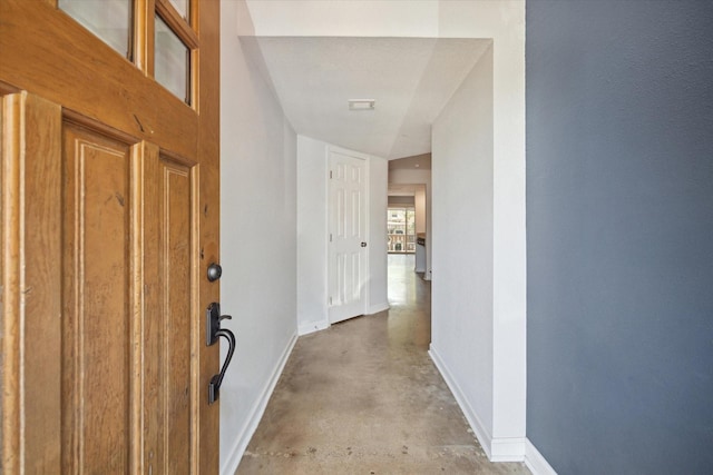 hall with visible vents, baseboards, and concrete flooring