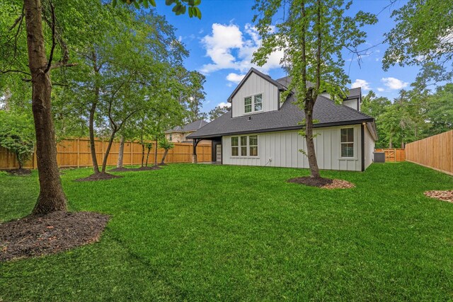 back of property featuring a lawn, a shingled roof, a fenced backyard, and central AC unit