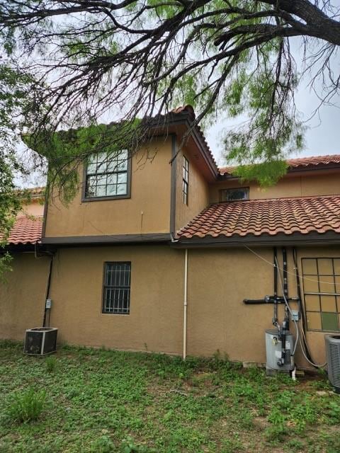 view of side of property featuring central AC, stucco siding, and a tiled roof