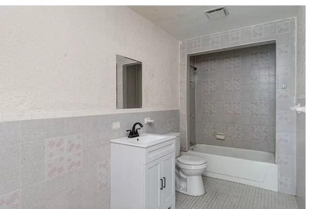 bathroom featuring tile patterned flooring, vanity, visible vents, toilet, and tile walls