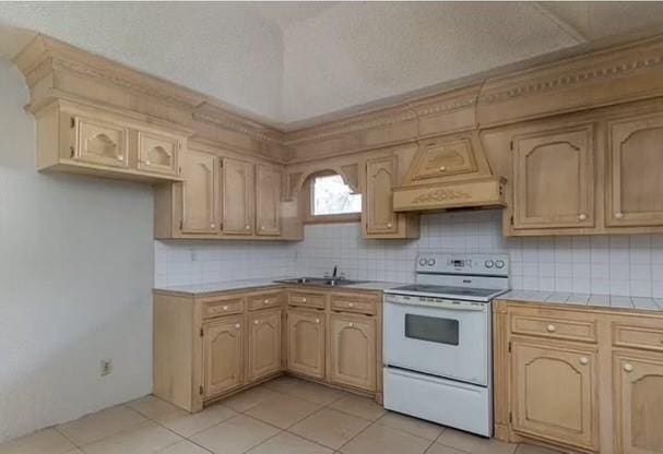 kitchen with custom exhaust hood, white electric range oven, tile counters, a sink, and backsplash