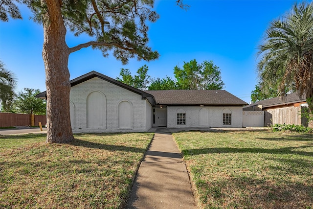 ranch-style home featuring brick siding, fence, and a front yard