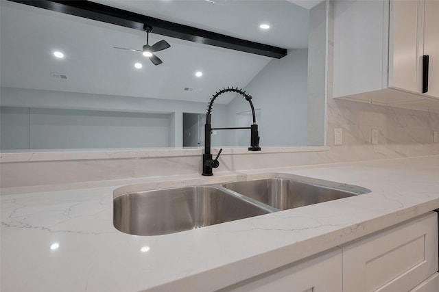 interior details with white cabinetry, a ceiling fan, light stone counters, and a sink
