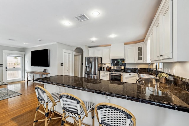 kitchen with appliances with stainless steel finishes, a breakfast bar, a sink, a peninsula, and visible vents