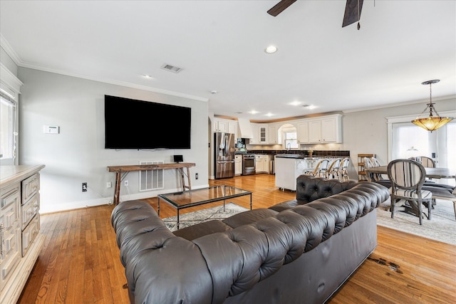 living room with crown molding, ceiling fan, light wood finished floors, and visible vents