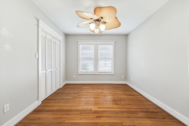 unfurnished bedroom featuring a closet, baseboards, ceiling fan, and wood finished floors