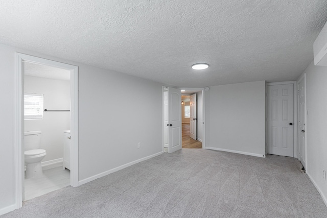 unfurnished bedroom with ensuite bath, carpet, a textured ceiling, and baseboards