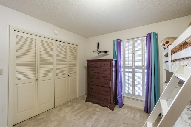 bedroom with a textured ceiling, a closet, baseboards, and light carpet