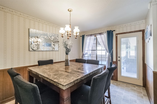 dining area featuring wainscoting, wallpapered walls, wooden walls, and a chandelier