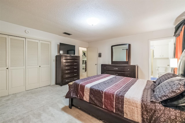 carpeted bedroom featuring ensuite bath, a textured ceiling, and visible vents