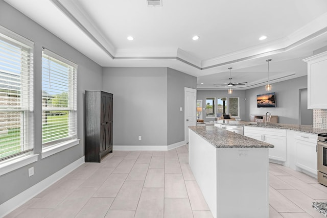 kitchen featuring plenty of natural light, a ceiling fan, a raised ceiling, and a sink