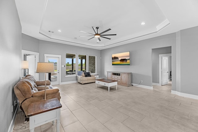 living area featuring a ceiling fan, a tray ceiling, recessed lighting, and baseboards