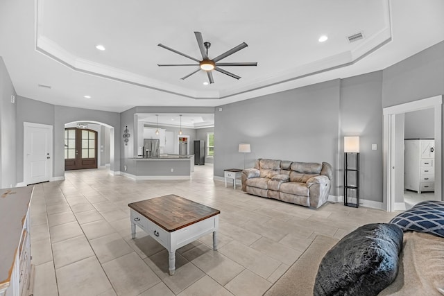 living room with ceiling fan, a raised ceiling, arched walkways, recessed lighting, and visible vents