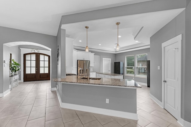 kitchen featuring stainless steel fridge, a sink, arched walkways, dark stone countertops, and white cabinetry