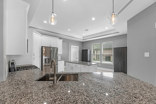 kitchen with stainless steel refrigerator with ice dispenser, a raised ceiling, white cabinetry, a sink, and dark stone countertops