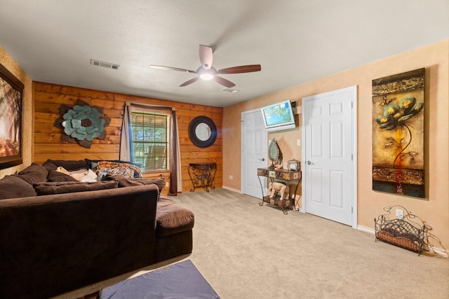 living room with ceiling fan, light carpet, baseboards, wood walls, and visible vents
