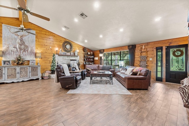 living area featuring wooden walls, vaulted ceiling, visible vents, wood finished floors, and a fireplace