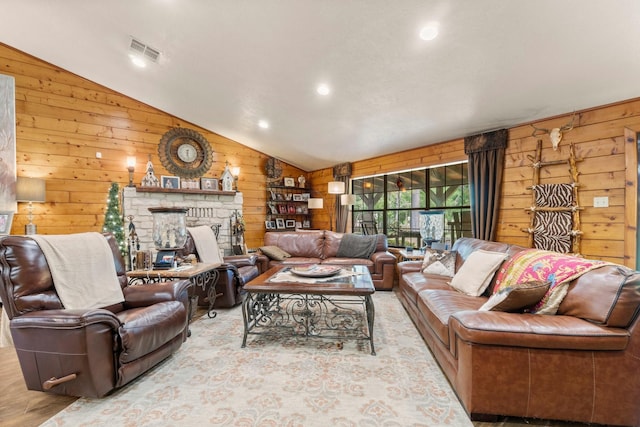 living area featuring wooden walls, lofted ceiling, a fireplace with raised hearth, and visible vents
