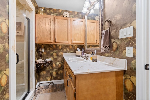 bathroom with wallpapered walls, wood finished floors, vanity, baseboards, and a stall shower