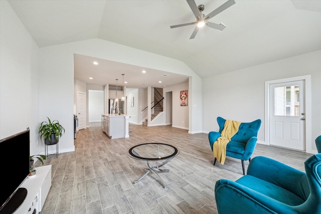 sitting room featuring a ceiling fan, light wood finished floors, vaulted ceiling, and stairs
