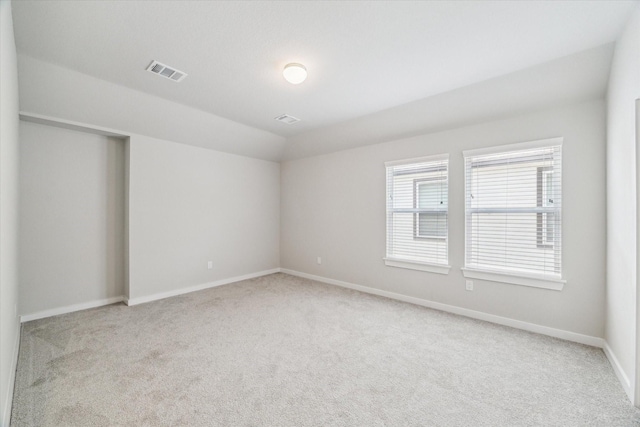 carpeted spare room featuring baseboards, visible vents, and lofted ceiling