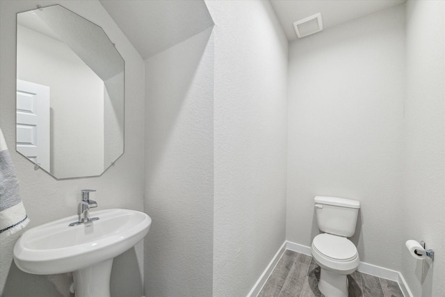 bathroom with a sink, wood tiled floor, visible vents, baseboards, and toilet
