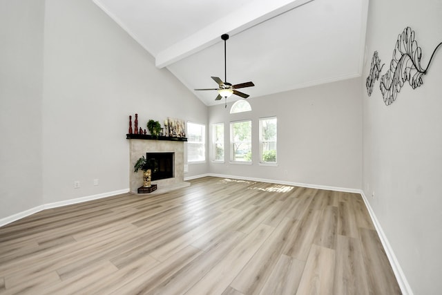 unfurnished living room featuring beam ceiling, light wood-style floors, a ceiling fan, baseboards, and a tile fireplace