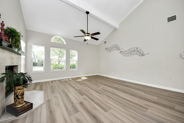 unfurnished living room with visible vents, beamed ceiling, ceiling fan, a tile fireplace, and light wood finished floors