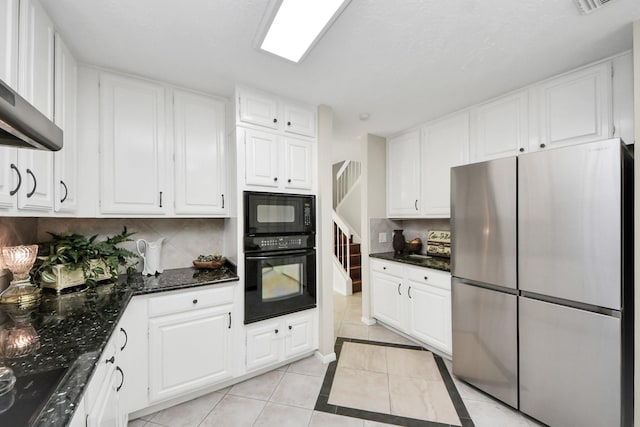 kitchen featuring decorative backsplash, light tile patterned flooring, white cabinets, dark stone countertops, and black appliances