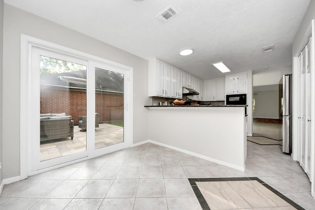 kitchen featuring white cabinets, dark countertops, freestanding refrigerator, under cabinet range hood, and visible vents