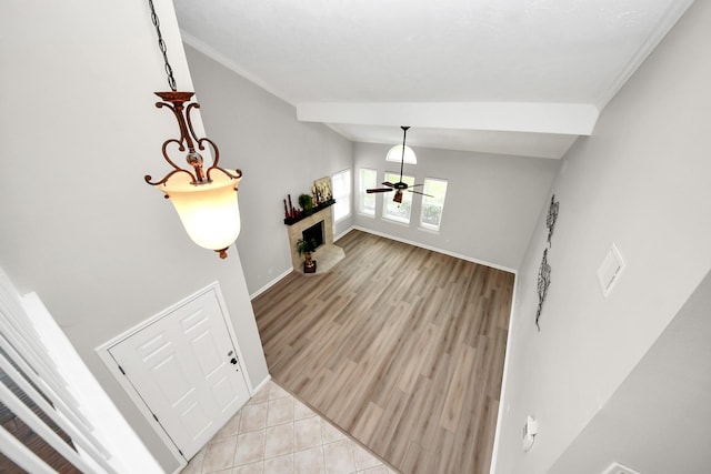 entryway featuring ceiling fan, light wood finished floors, a fireplace with raised hearth, baseboards, and vaulted ceiling
