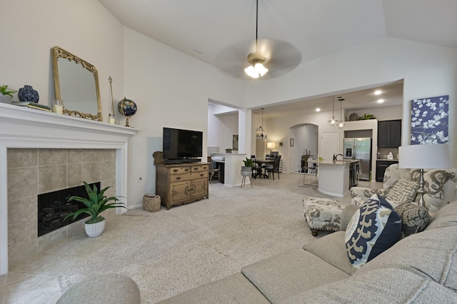 living area featuring a tile fireplace, high vaulted ceiling, arched walkways, and ceiling fan with notable chandelier