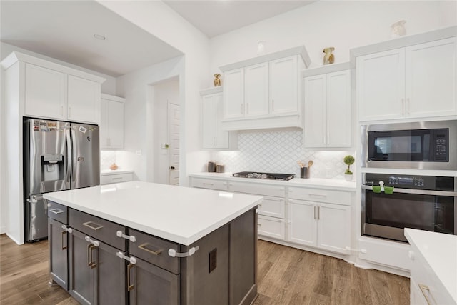 kitchen with wood finished floors, stainless steel appliances, light countertops, backsplash, and white cabinetry