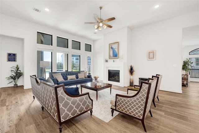 living area featuring a glass covered fireplace, wood finished floors, a healthy amount of sunlight, and a ceiling fan