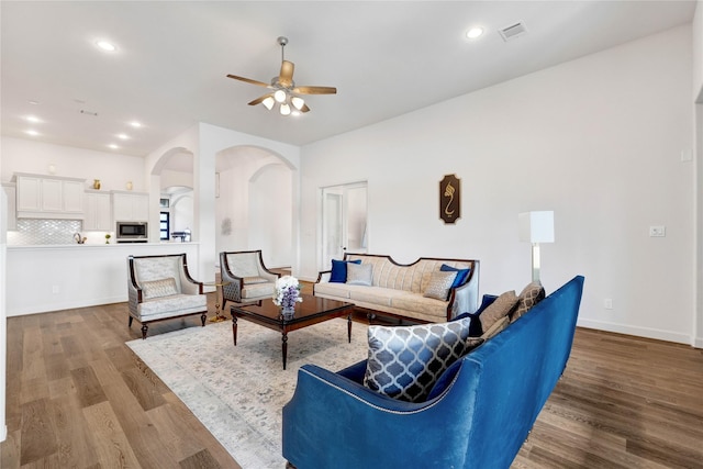 living room featuring ceiling fan, arched walkways, wood finished floors, and visible vents