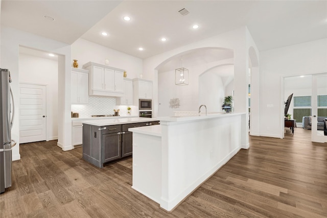 kitchen featuring decorative backsplash, arched walkways, stainless steel appliances, light countertops, and dark wood-style floors