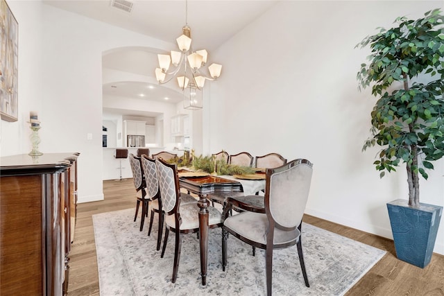 dining area featuring arched walkways, baseboards, visible vents, an inviting chandelier, and light wood-style floors