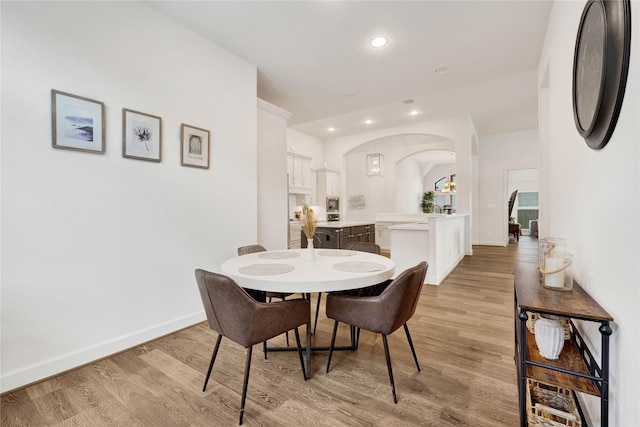 dining area featuring baseboards, arched walkways, light wood-style flooring, and recessed lighting