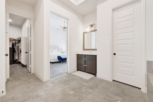 full bathroom featuring a ceiling fan, vanity, a walk in closet, ensuite bath, and baseboards