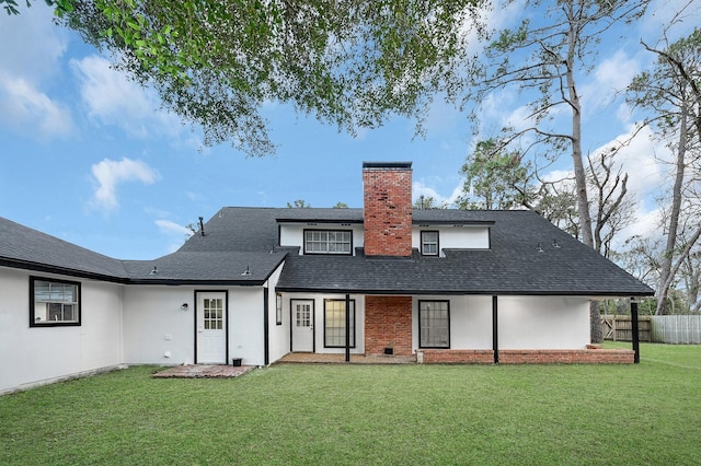 back of house with a lawn, a chimney, a shingled roof, fence, and stucco siding