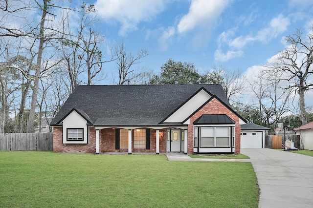 view of front facade with roof with shingles, concrete driveway, fence, brick siding, and a front yard