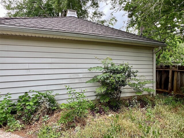 view of home's exterior featuring fence, a shingled roof, and a chimney