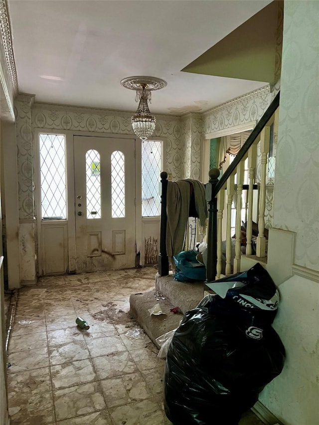 foyer featuring a chandelier, wallpapered walls, and stairs