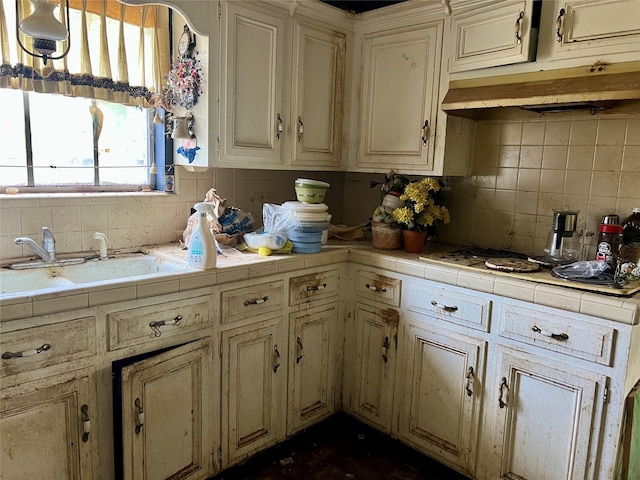 kitchen featuring a sink, tile countertops, white cooktop, backsplash, and under cabinet range hood
