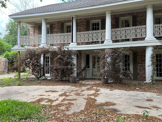 view of front of property with a balcony, a shingled roof, and brick siding