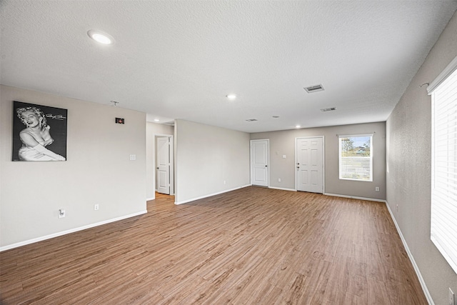 unfurnished living room featuring light wood-style floors, a textured ceiling, baseboards, and visible vents