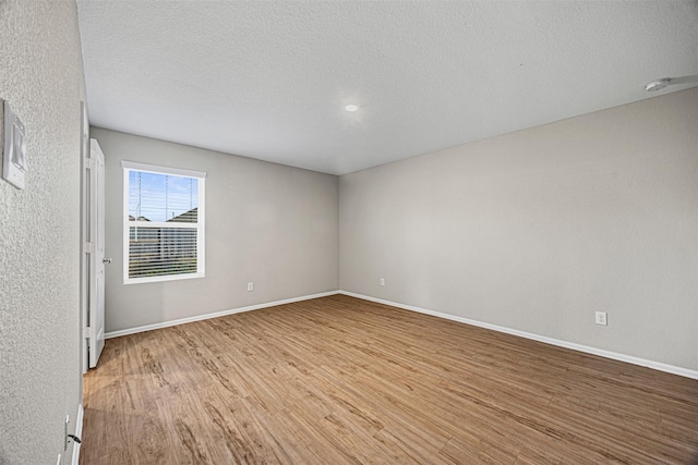 unfurnished room with baseboards, a textured ceiling, and light wood finished floors