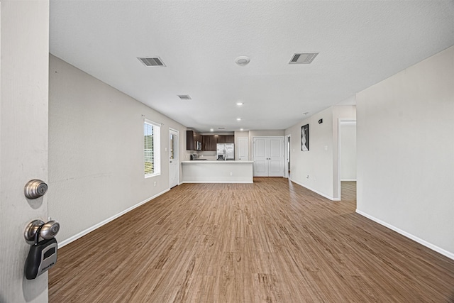 unfurnished living room featuring light wood-style flooring, visible vents, and baseboards